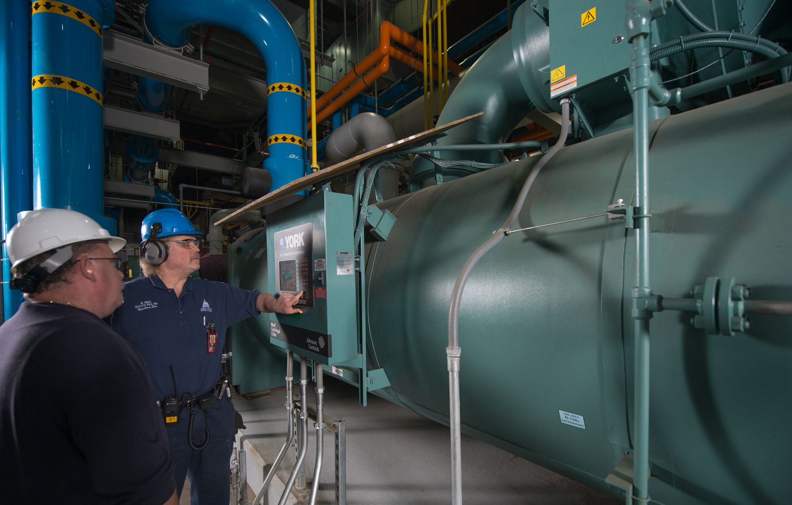 Chiller de água gelada em sala de máquinas, com técnicos operando o painel de controle